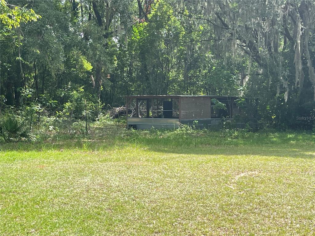 A small, weathered shed with a metal roof sits in a grassy, wooded yard — 8095 SE 131ST PLACE, SUMMERFIELD, FL