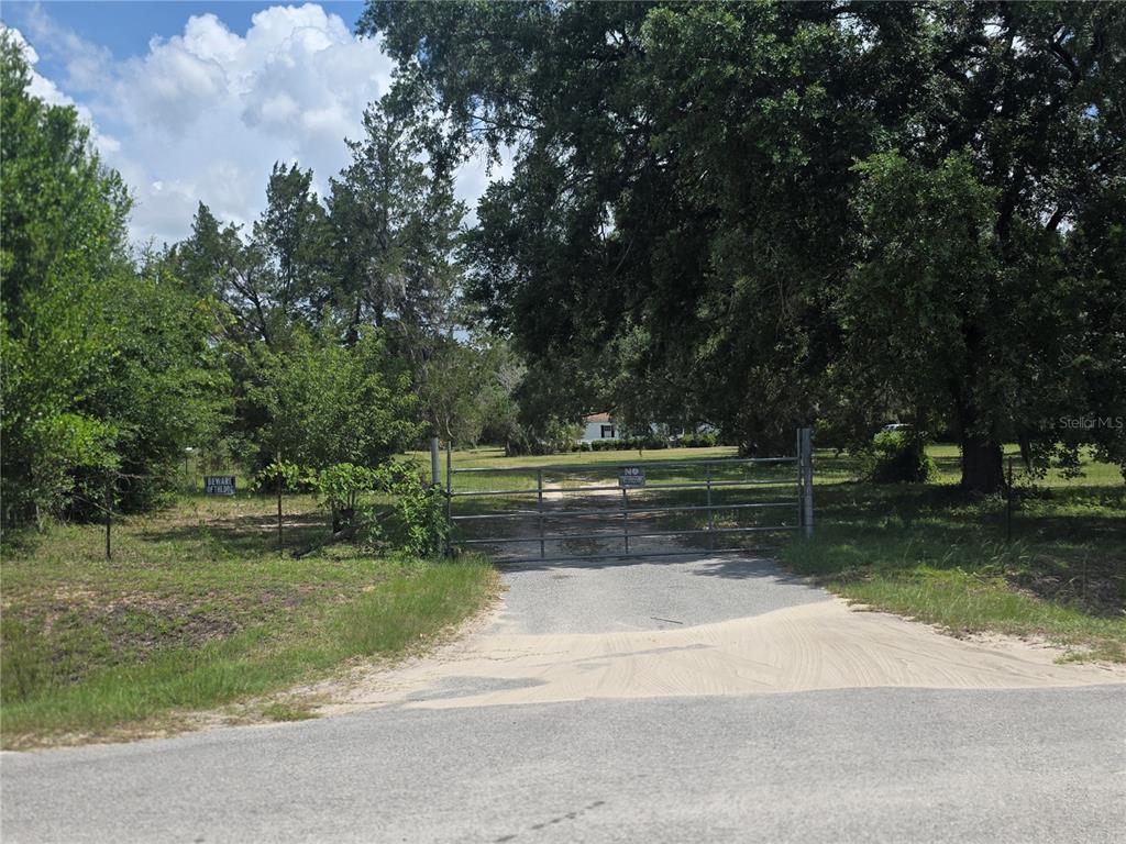 A metal gate blocks a gravel driveway leading to a house surrounded by large trees — 8095 SE 131ST PLACE, SUMMERFIELD, FL