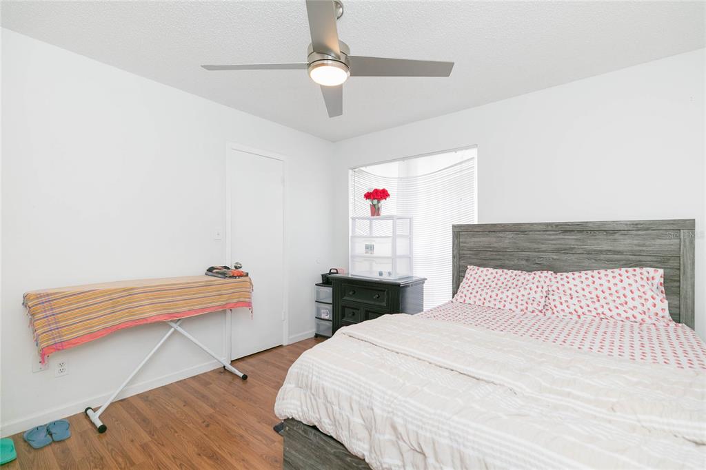 A bedroom features wood-look flooring, a ceiling fan, a bed with a gray headboard, and an ironing board — 8636 MALLARD RESERVE DRIVE UNIT 201, TAMPA, FL