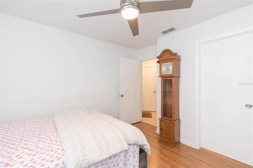 A bedroom features wood-look flooring, a ceiling fan, and a tall wooden grandfather clock — 8636 MALLARD RESERVE DRIVE UNIT 201, TAMPA, FL