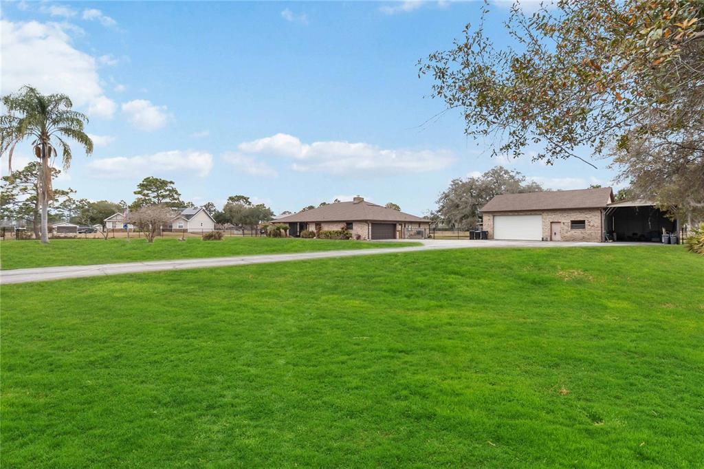 A grassy yard leads to a brick house and a detached garage under a blue sky — 18711 NORTHCLIFF STREET, ORLANDO, FL