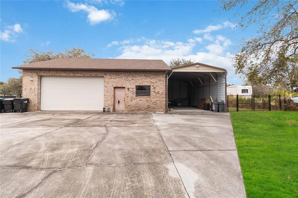 A brick garage with a roll-up door, a side entrance, and an attached metal carport — 18711 NORTHCLIFF STREET, ORLANDO, FL