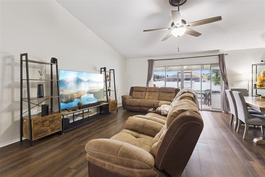 A living room features brown reclining sofas, a large television, and dark wood flooring — 7973 OAK RUN CIRCLE, LAKELAND, FL