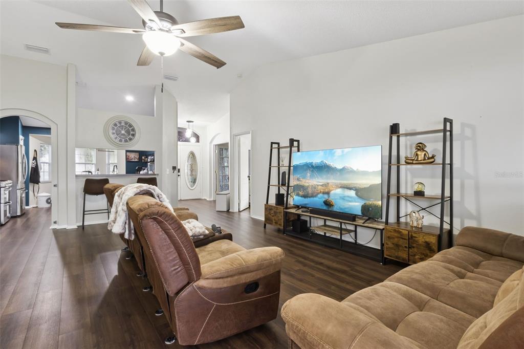 A living room features brown reclining sofas, a large television, and dark wood-look flooring — 7973 OAK RUN CIRCLE, LAKELAND, FL