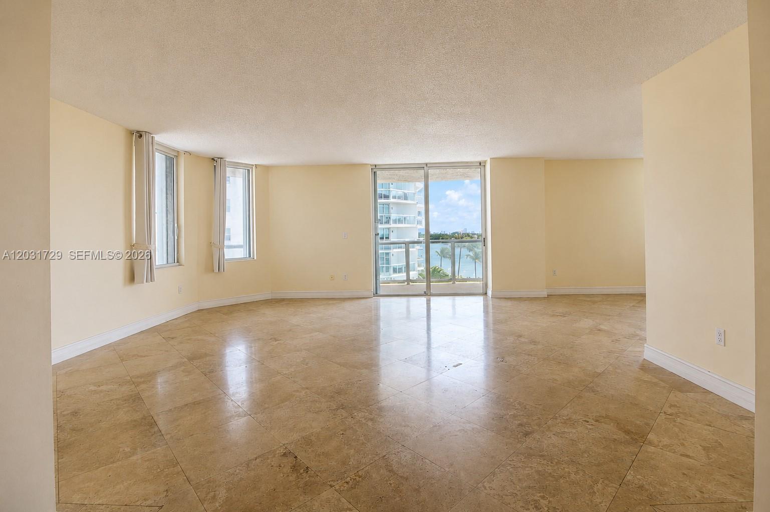 An empty living room features beige tile floors, light-colored walls, and a balcony with water views — 5900 Collins Ave # 601, Miami Beach FL 33140, MIAMI BEACH, FL