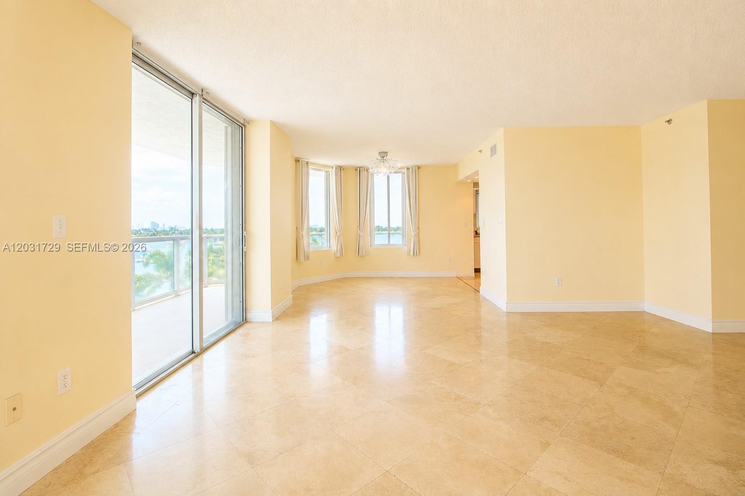 An empty living room features light yellow walls, beige tile flooring, and a glass balcony door — 5900 Collins Ave # 601, Miami Beach FL 33140, MIAMI BEACH, FL