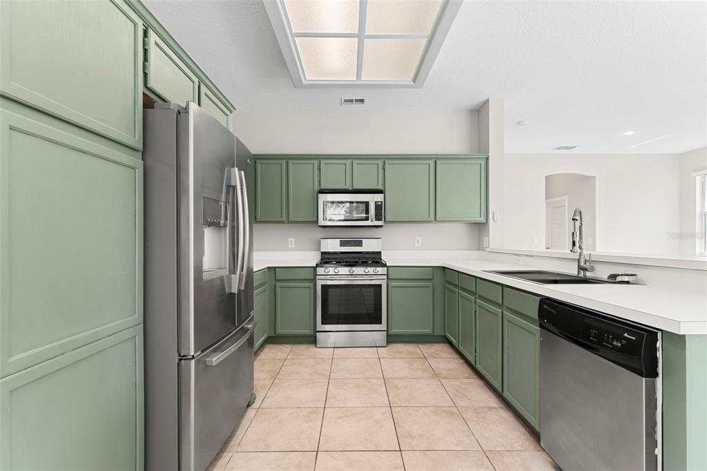 A kitchen with sage green cabinets, stainless steel appliances, and light-colored tile flooring — 315 SUNCREST COURT, OVIEDO, FL