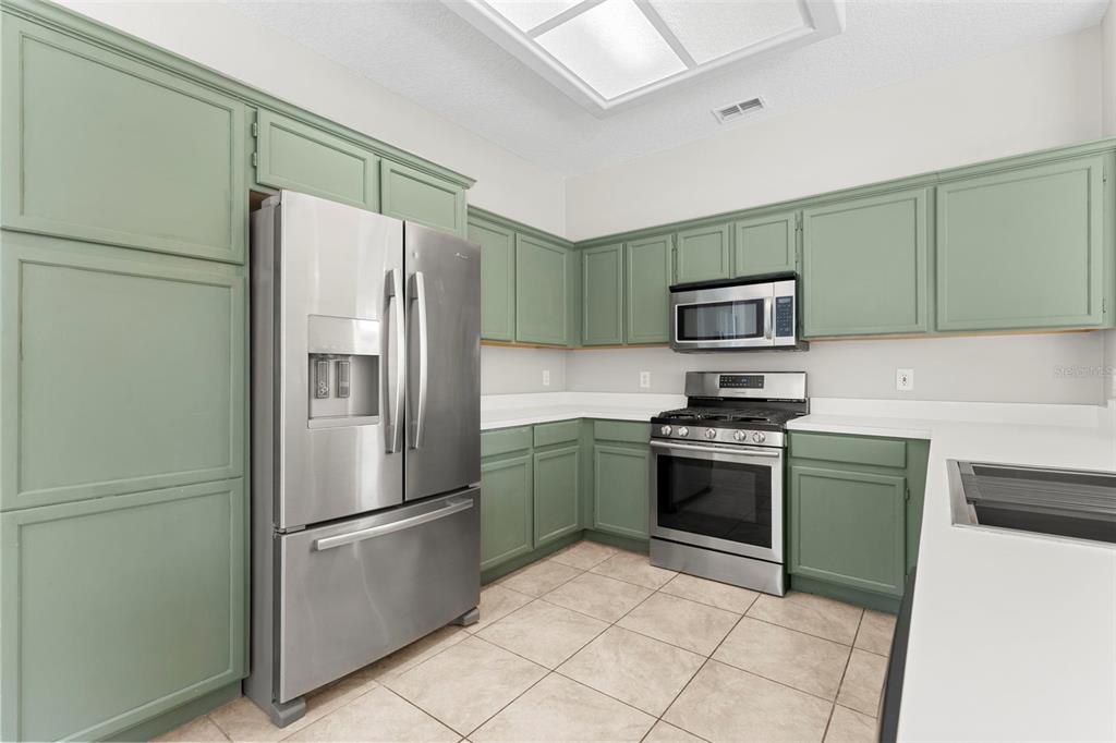 A kitchen features sage green cabinets, stainless steel appliances, white countertops, and tiled flooring — 315 SUNCREST COURT, OVIEDO, FL