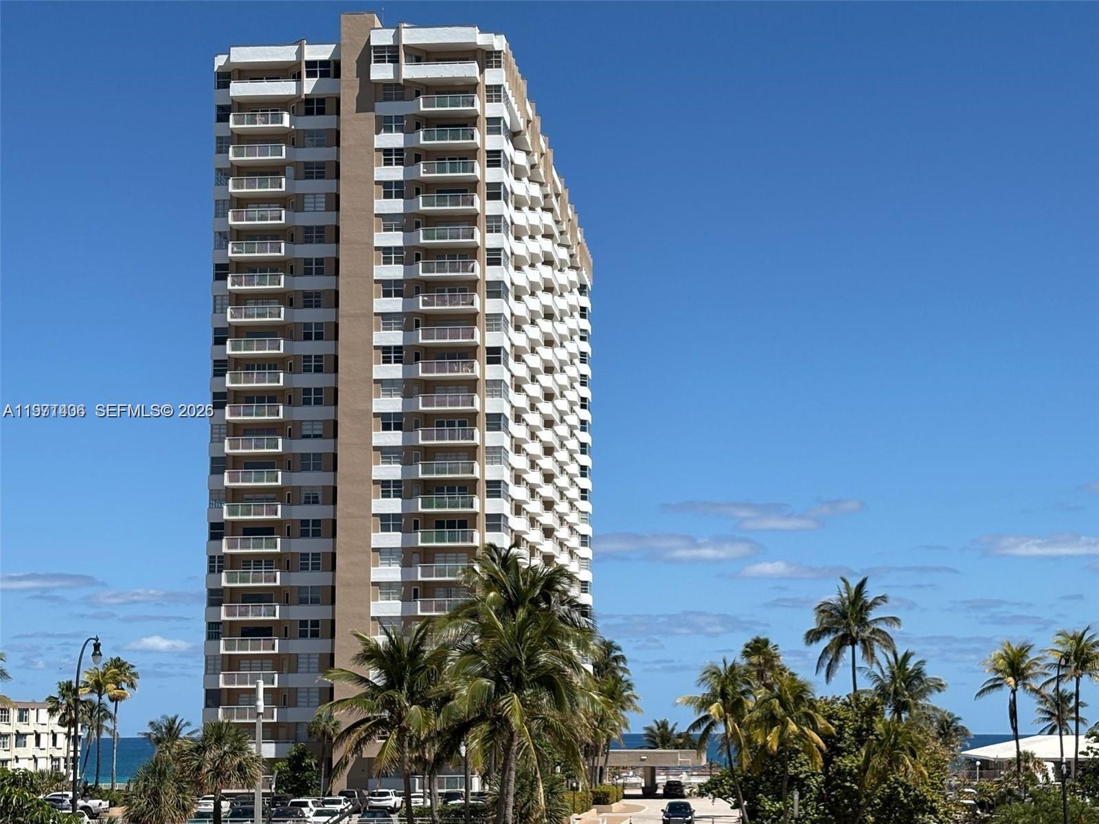 A tall, multi-story residential building stands near palm trees under a clear blue sky — 1965 S Ocean Dr # 2F, Hallandale Beach FL 33009, HALLANDALE BEACH, FL