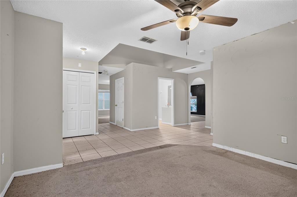 A room with beige carpet, tiled flooring, a ceiling fan, and several interior doorways — 12803 LAKE VISTA DRIVE, GIBSONTON, FL