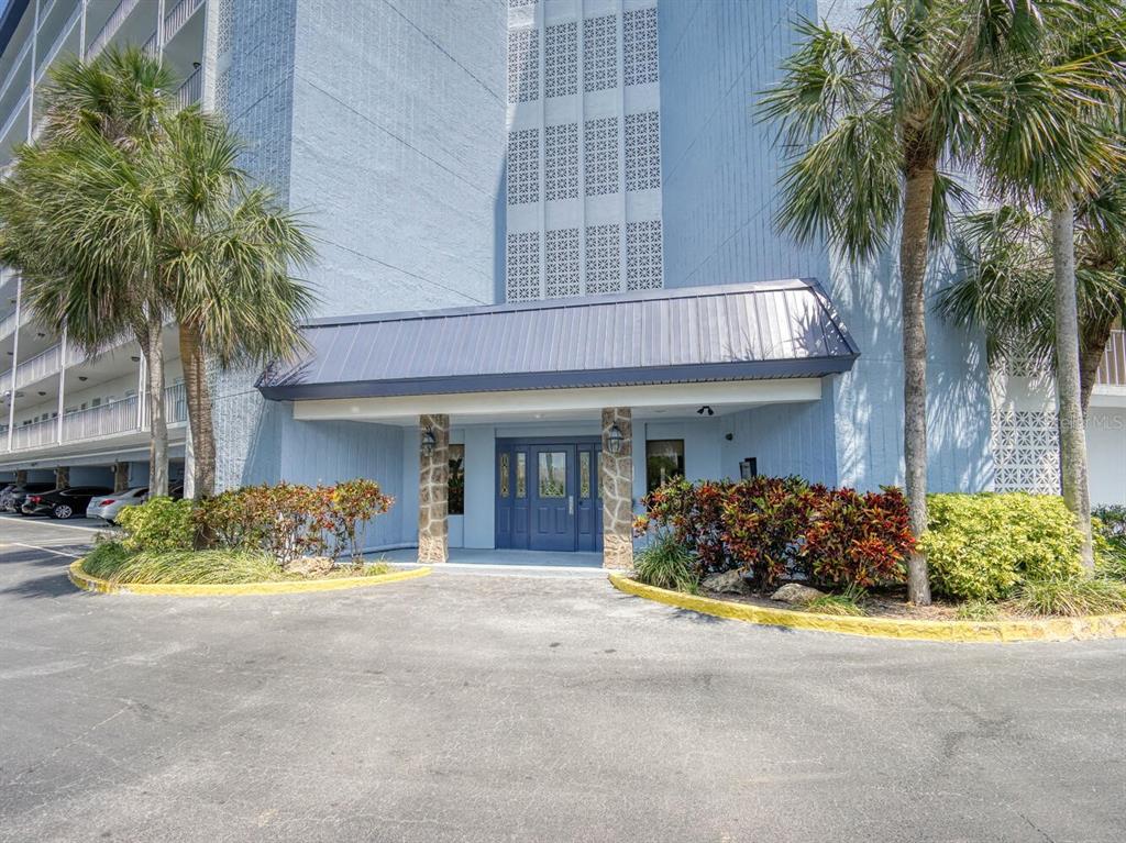 The exterior of a blue building features a covered entrance with stone pillars and palm trees — 4939 FLORAMAR TERRACE UNIT 904, NEW PORT RICHEY, FL