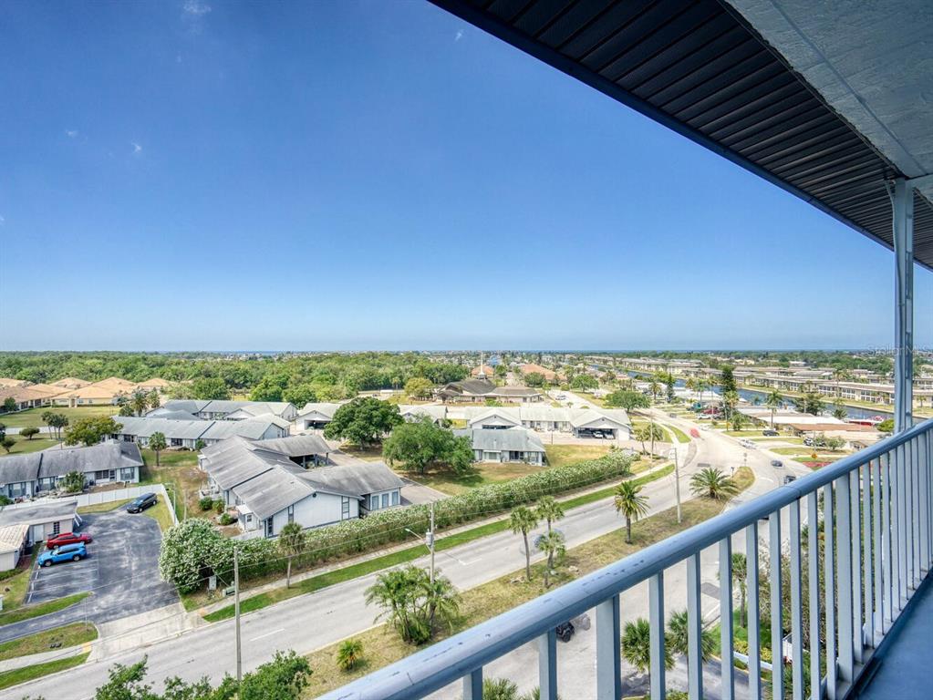 An elevated view from a balcony overlooking a suburban neighborhood, a road, and distant trees — 4939 FLORAMAR TERRACE UNIT 904, NEW PORT RICHEY, FL
