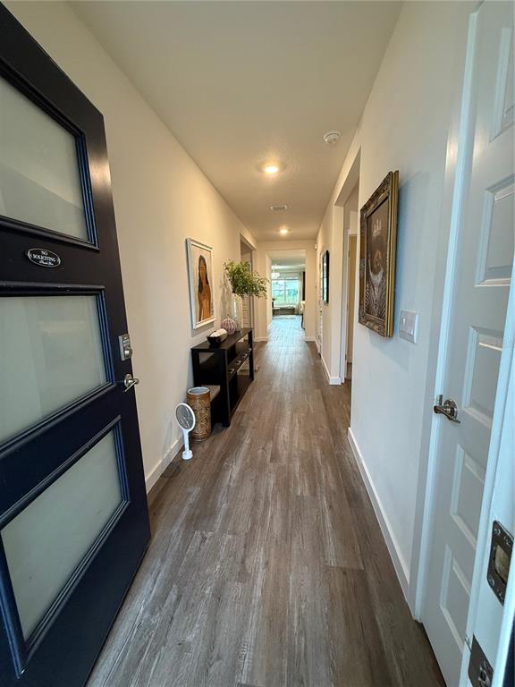 A long hallway with wood-look flooring leads from a dark front door toward a living area — 31800 OYSTER TRELLIS LANE, WESLEY CHAPEL, FL