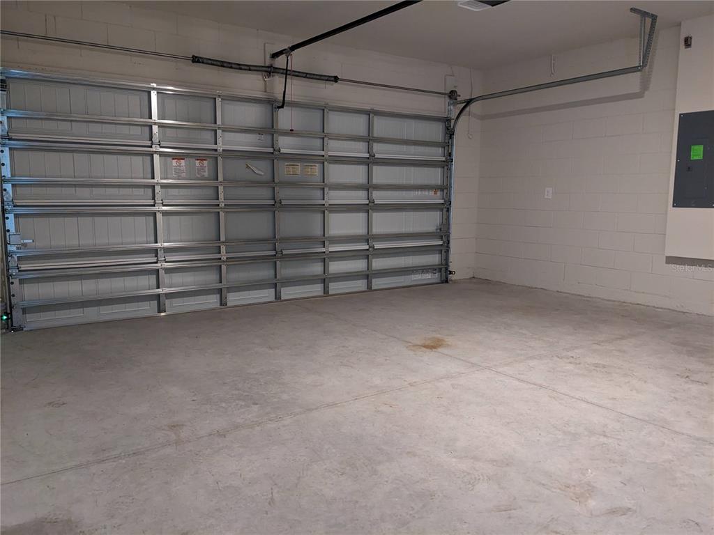 An empty garage with a concrete floor, white block walls, and a metal sectional door — 1113 GRAND HAMMOCK COURT, KISSIMMEE, FL