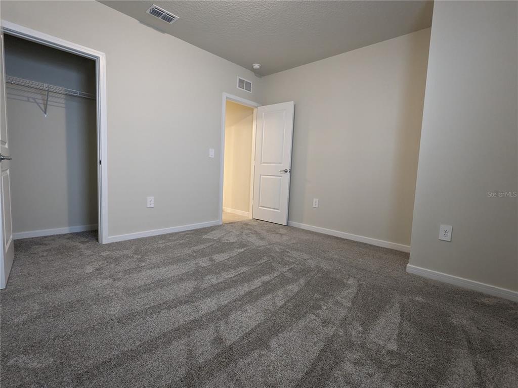 An empty bedroom features gray carpeting, beige walls, a walk-in closet, and an open doorway — 1113 GRAND HAMMOCK COURT, KISSIMMEE, FL