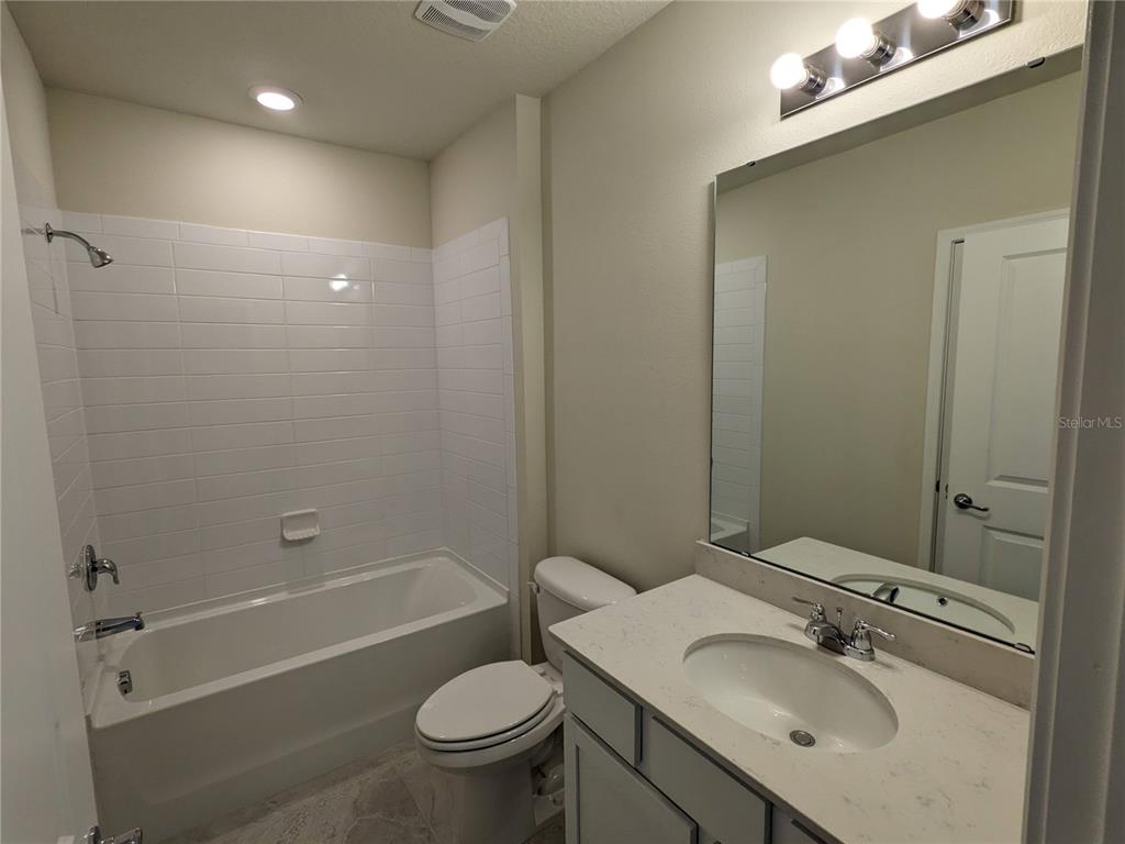 A bathroom features a white subway-tiled shower-tub combo, a toilet, and a single-sink vanity — 1113 GRAND HAMMOCK COURT, KISSIMMEE, FL