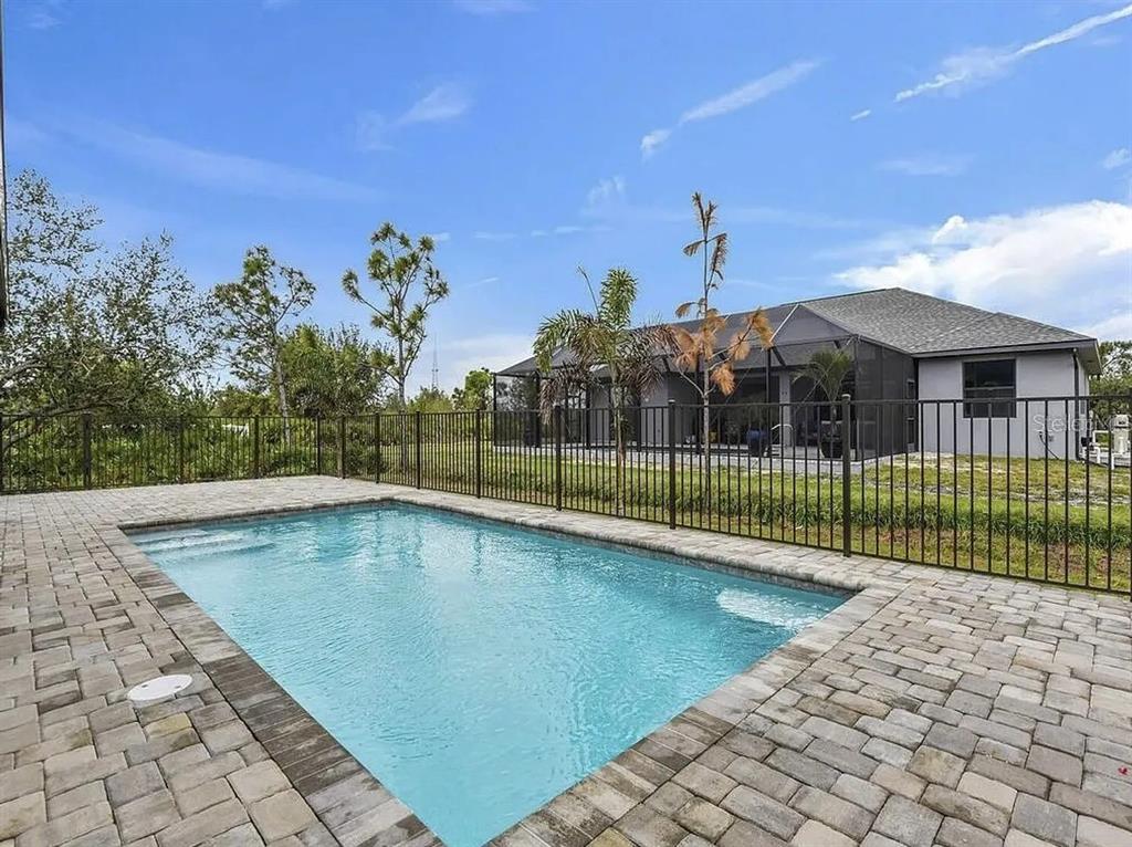 A rectangular swimming pool with a paver deck is enclosed by a black metal fence — 9307 CYCLAMEN STREET, PORT CHARLOTTE, FL