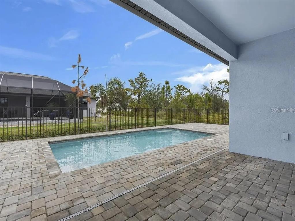 A rectangular swimming pool sits on a paved patio beside a house with a fence — 9307 CYCLAMEN STREET, PORT CHARLOTTE, FL