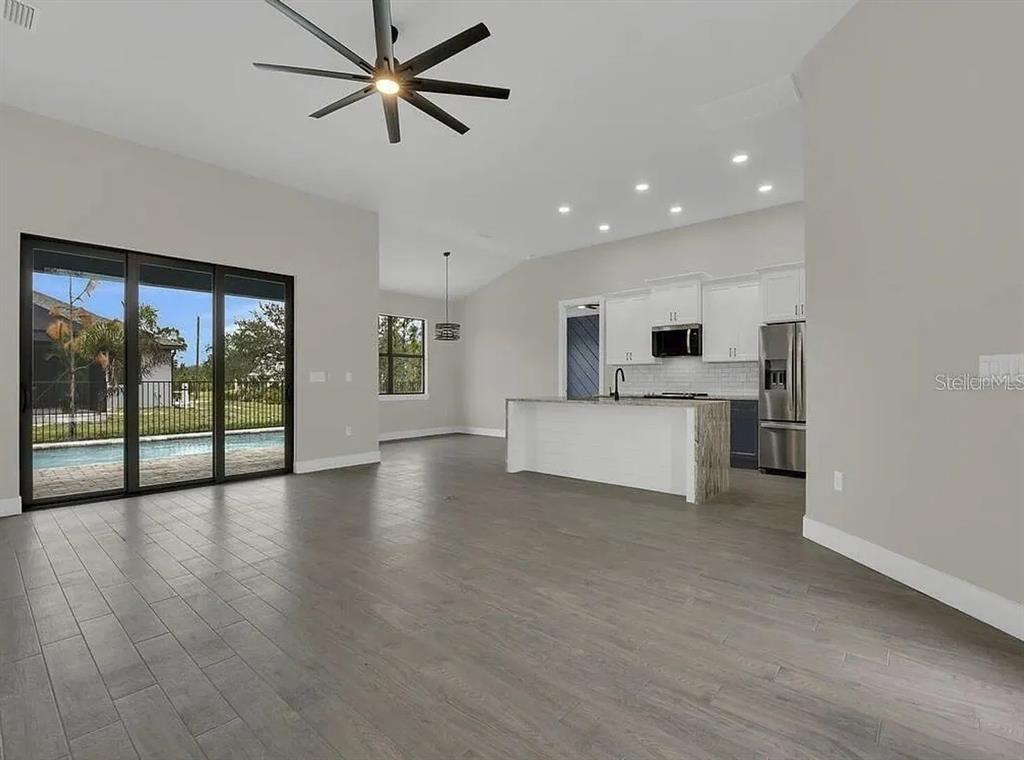 A bright open-concept living area features gray tile flooring, a kitchen island, and sliding glass doors — 9307 CYCLAMEN STREET, PORT CHARLOTTE, FL