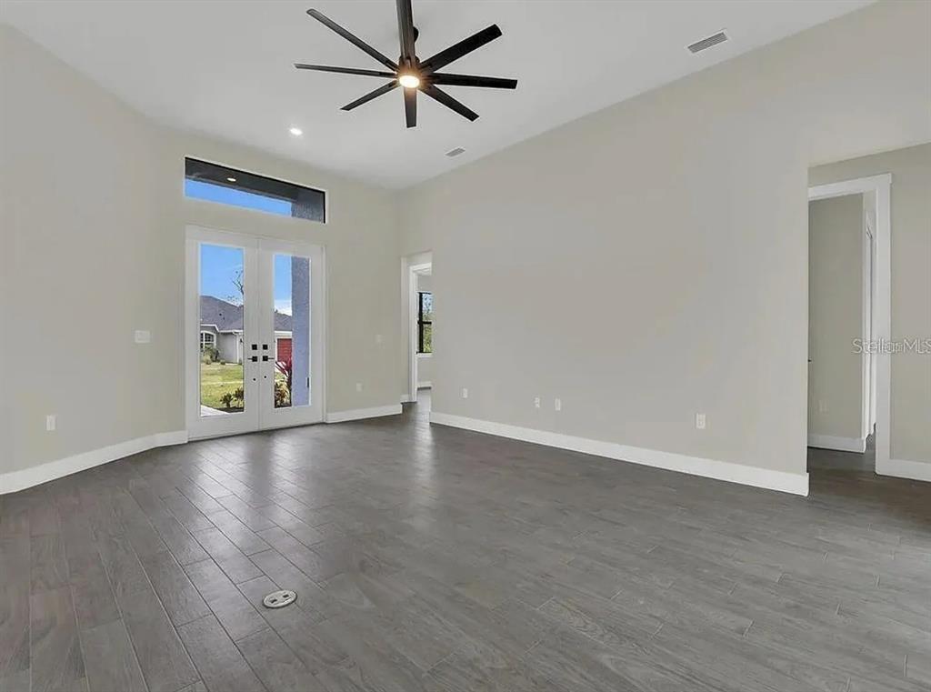 An empty room with gray wood-look flooring, a ceiling fan, and double glass doors — 9307 CYCLAMEN STREET, PORT CHARLOTTE, FL