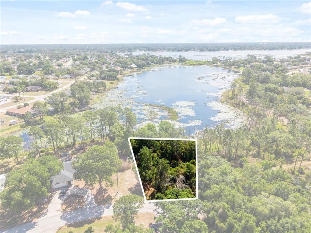 An aerial view shows a wooded lot highlighted against a lake and residential neighborhood — 1351 MELSHIRE AVENUE, DELTONA, FL