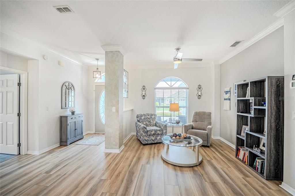A living room features wood-look flooring, a ceiling fan, a window, and a bookshelf — 8371 SW 84TH LOOP, OCALA, FL