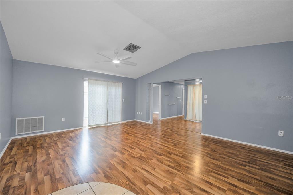 A spacious living room features light blue walls, wood-look flooring, and a vaulted ceiling — 13005 CLUB DRIVE, HUDSON, FL
