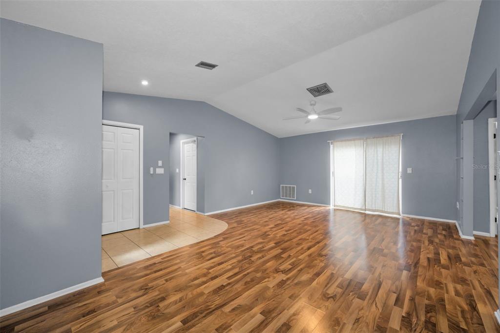 A living room with vaulted ceilings, wood-look flooring, a ceiling fan, and sliding glass doors — 13005 CLUB DRIVE, HUDSON, FL