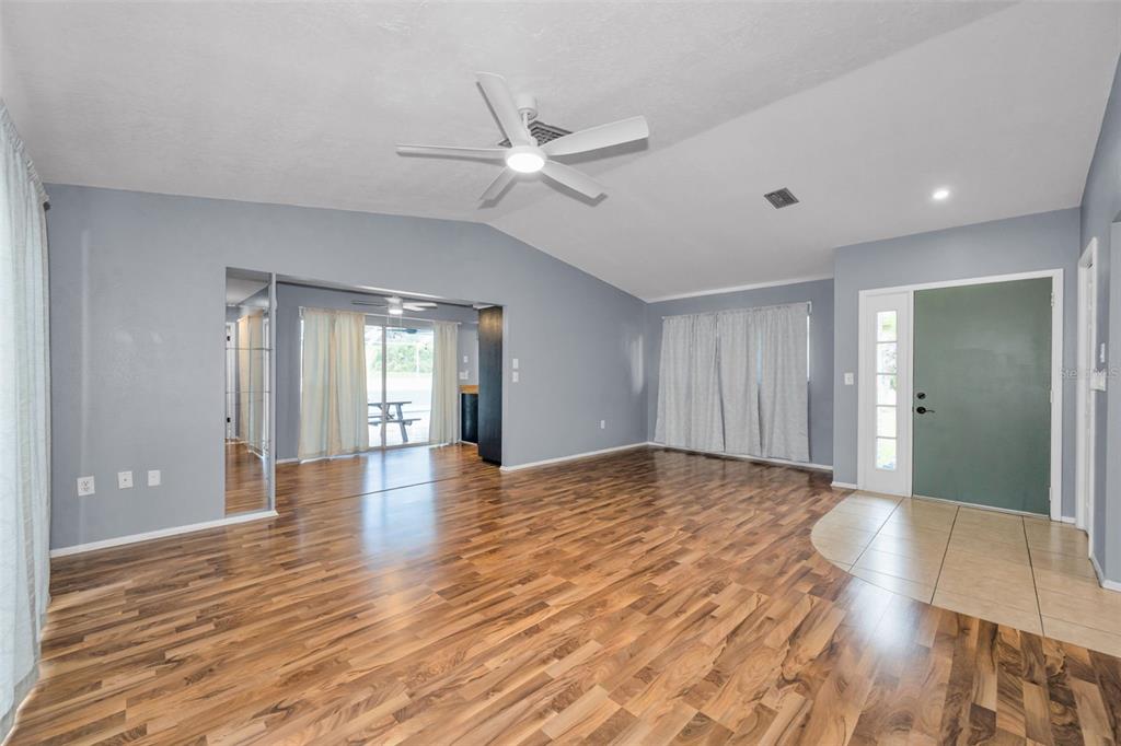 A living room with wood-look flooring, a vaulted ceiling, a ceiling fan, and a front door — 13005 CLUB DRIVE, HUDSON, FL