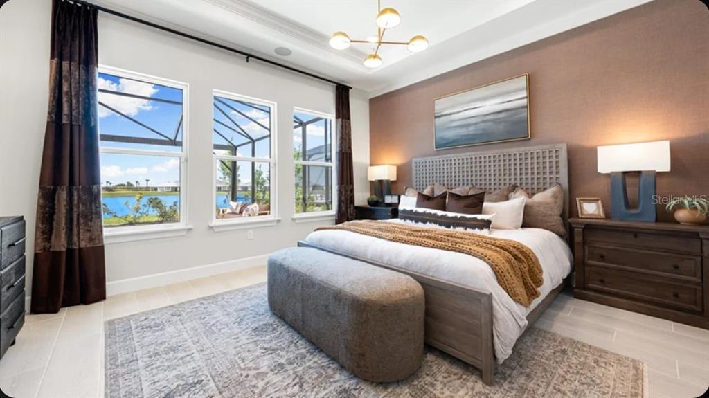 A bedroom features a king bed, textured accent wall, and large windows overlooking a lake — 17742 SEDONA STREET, WINTER GARDEN, FL