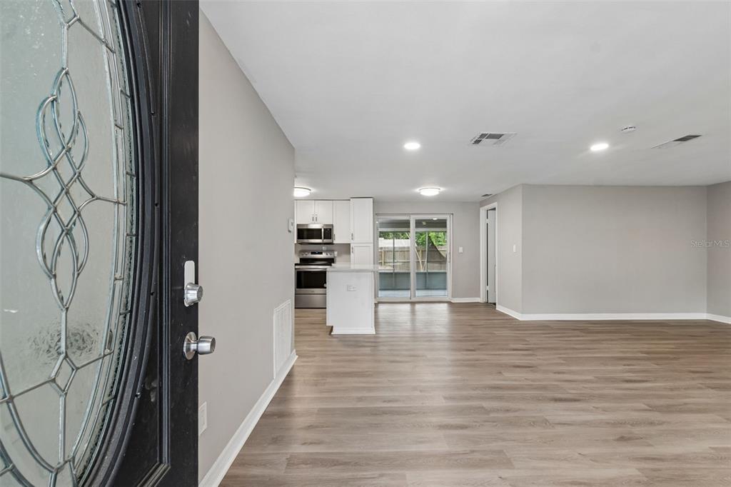 An open-concept living area features light wood-look flooring, a kitchen with white cabinets, and sliding doors — 1124 JADEWOOD AVENUE, CLEARWATER, FL