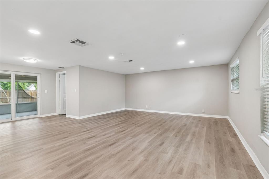 An empty living room features light wood-look flooring, recessed lighting, and a sliding glass door — 1124 JADEWOOD AVENUE, CLEARWATER, FL