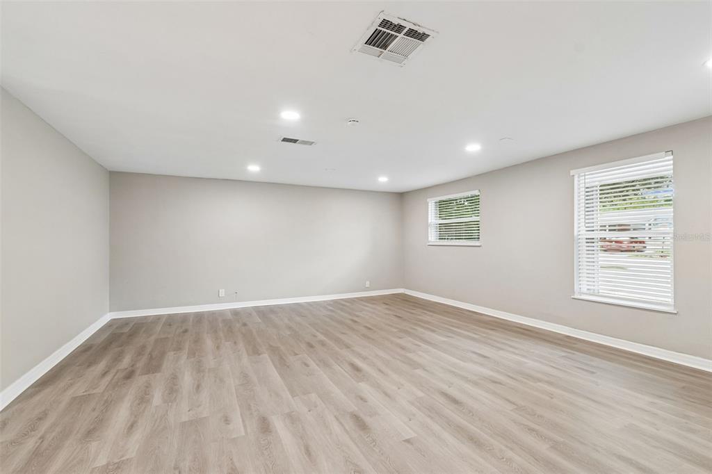 A living room features light wood-look flooring, a beige sofa, two armchairs, and a rug — 1124 JADEWOOD AVENUE, CLEARWATER, FL