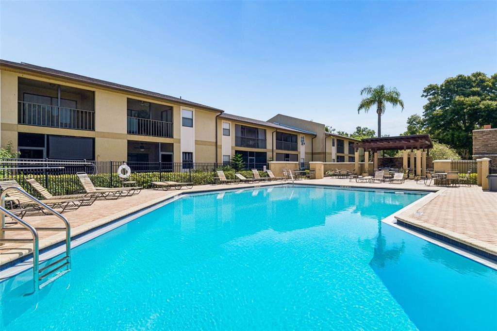 A swimming pool with lounge chairs sits in front of a multi-story apartment building — 10100 SAILWINDS BOULEVARD N UNIT 202, LARGO, FL