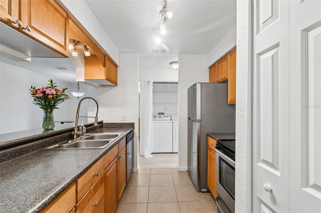 A galley kitchen features wood cabinets, granite countertops, stainless steel appliances, and a laundry area — 10100 SAILWINDS BOULEVARD N UNIT 202, LARGO, FL