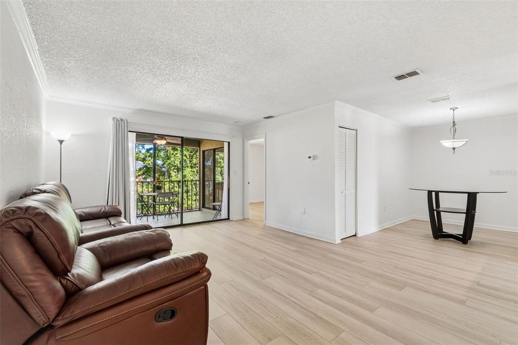 A living and dining area with light wood flooring, white walls, and a sliding glass door — 10100 SAILWINDS BOULEVARD N UNIT 202, LARGO, FL