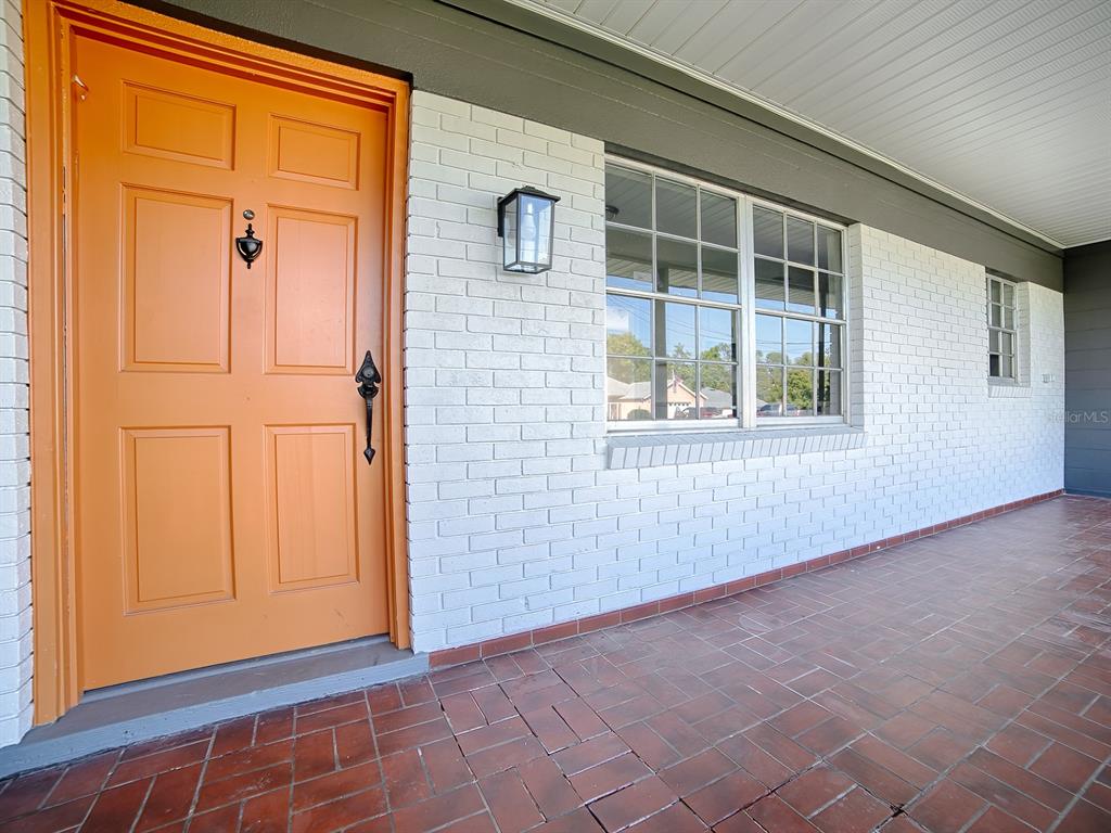 A bright orange front door sits next to a white brick wall and tiled porch — 5 OAK STREET, YALAHA, FL