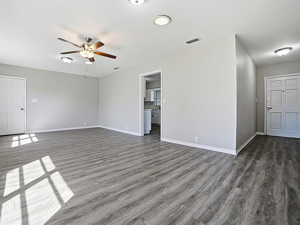 An empty living room with gray wood-look flooring, a ceiling fan, and a white door — 5 OAK STREET, YALAHA, FL