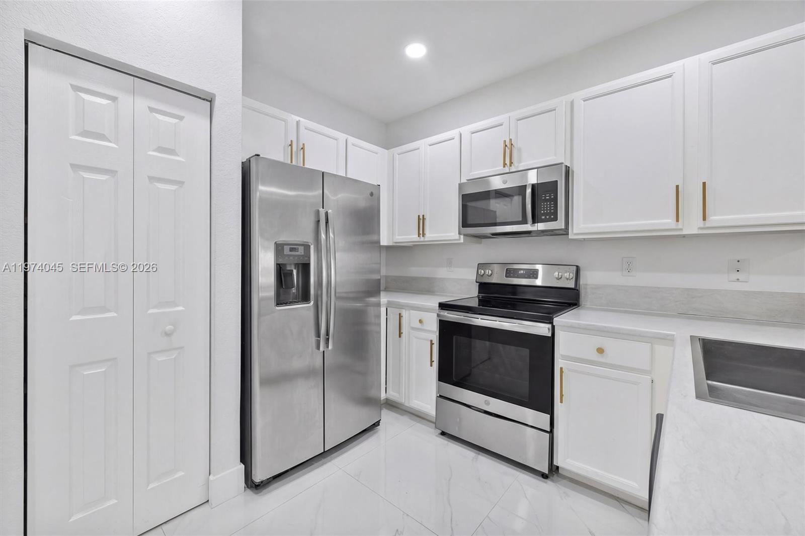 A kitchen features white cabinets, stainless steel appliances, and light-colored countertops — 178 SE 33rd Ter, Homestead FL 33033, HOMESTEAD, FL