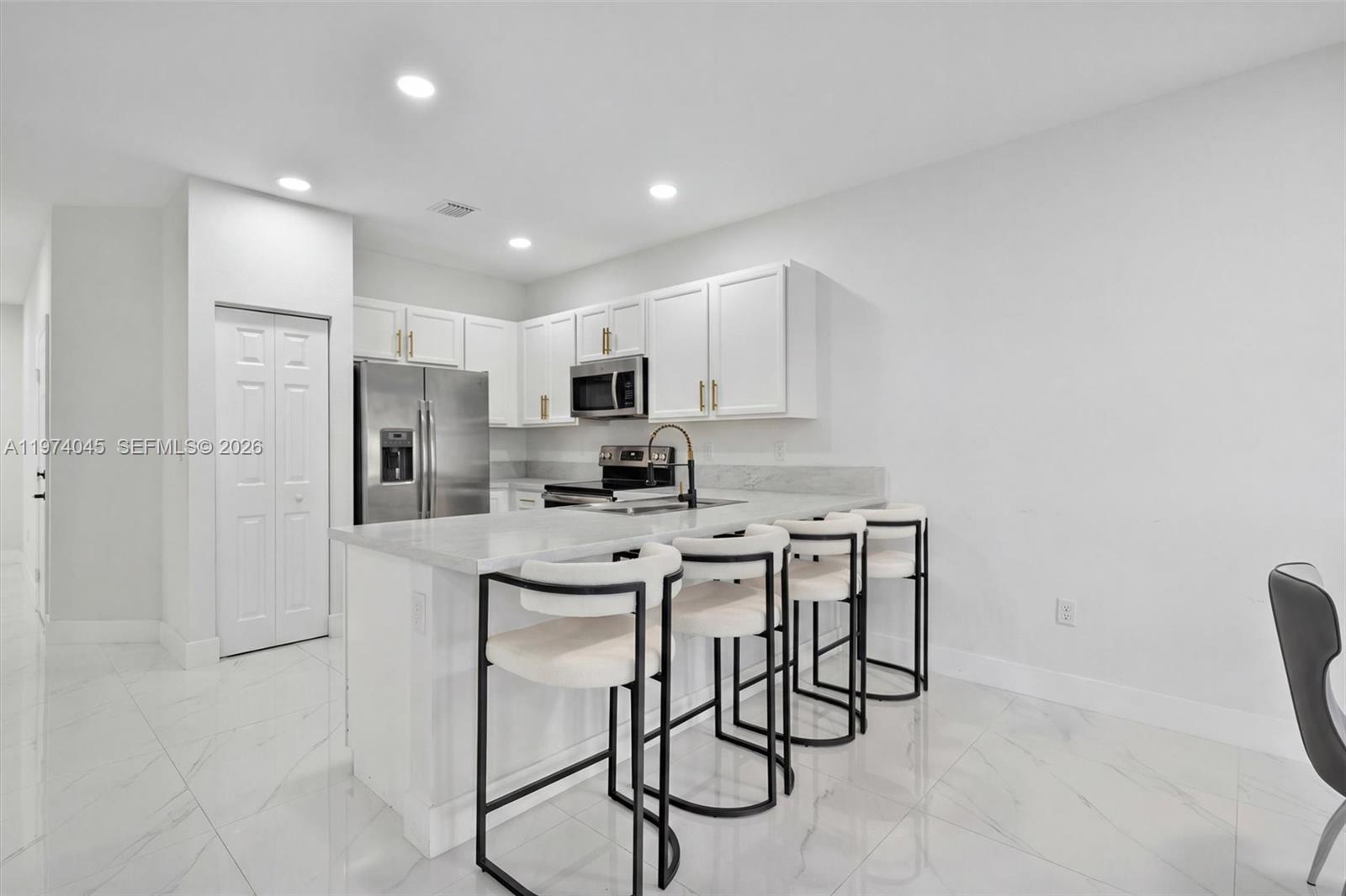 A modern kitchen features white cabinets, stainless steel appliances, a marble-topped island, and bar stools — 178 SE 33rd Ter, Homestead FL 33033, HOMESTEAD, FL
