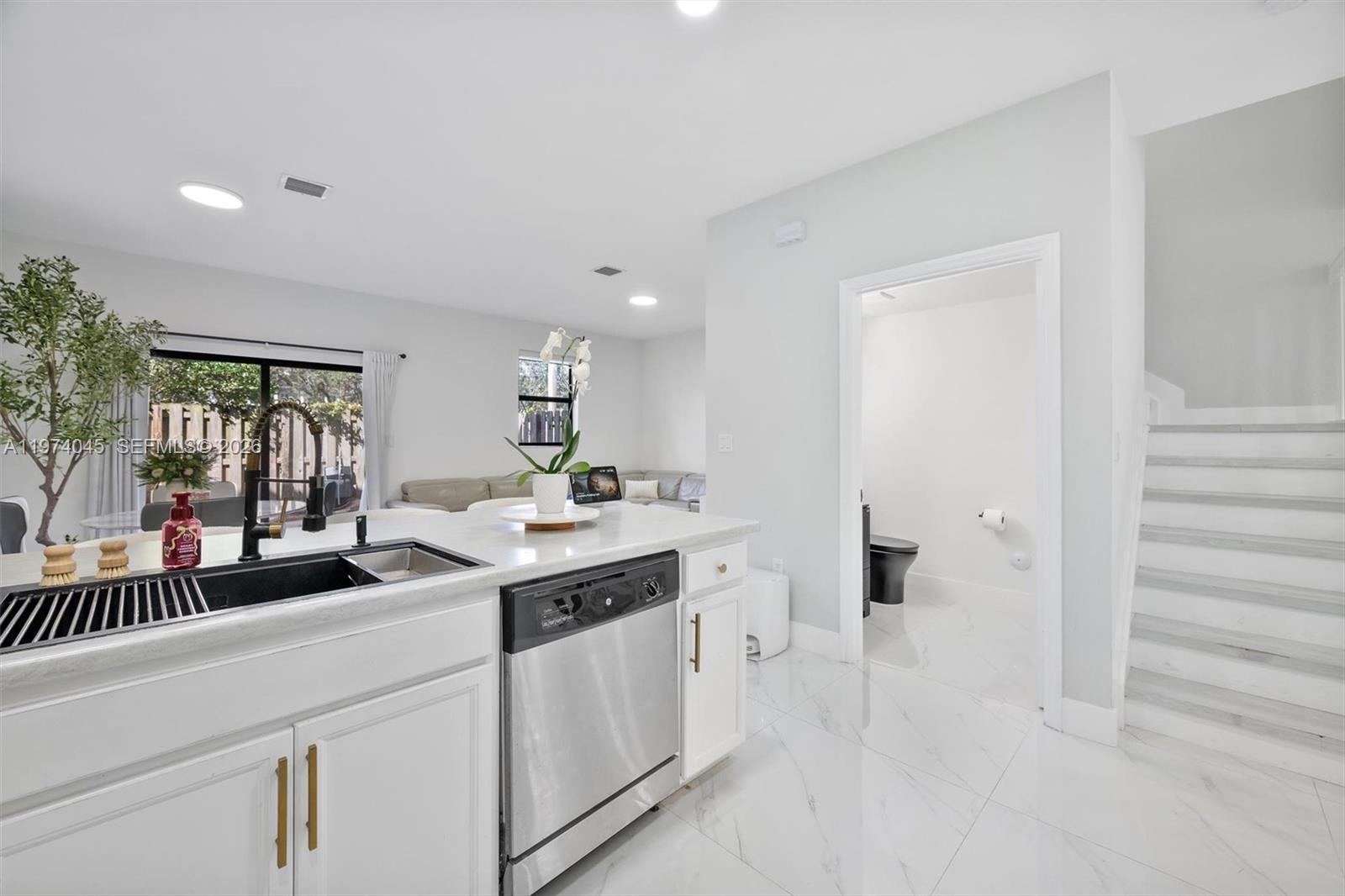 A modern kitchen with white cabinets, a stainless dishwasher, and a view of stairs — 178 SE 33rd Ter, Homestead FL 33033, HOMESTEAD, FL