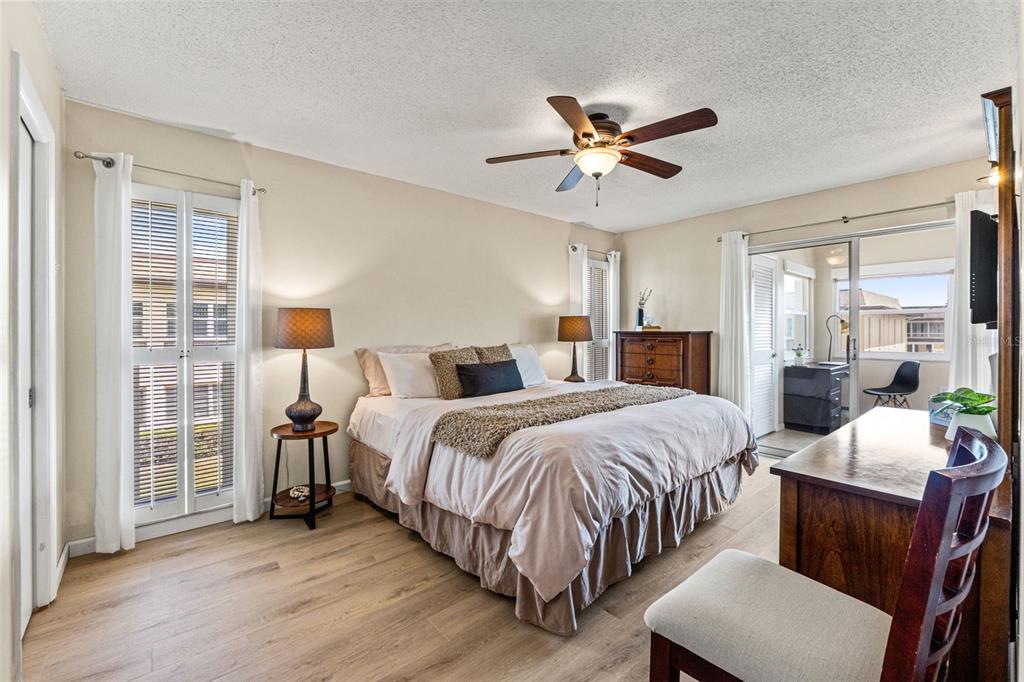 A bedroom features a bed, ceiling fan, wood-look flooring, and a sliding door to a balcony — 5111 AMULET DRIVE UNIT 202, NEW PORT RICHEY, FL