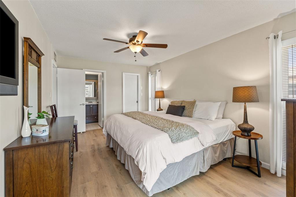 A bedroom features a king bed, wood-look flooring, a ceiling fan, and an attached bathroom — 5111 AMULET DRIVE UNIT 202, NEW PORT RICHEY, FL