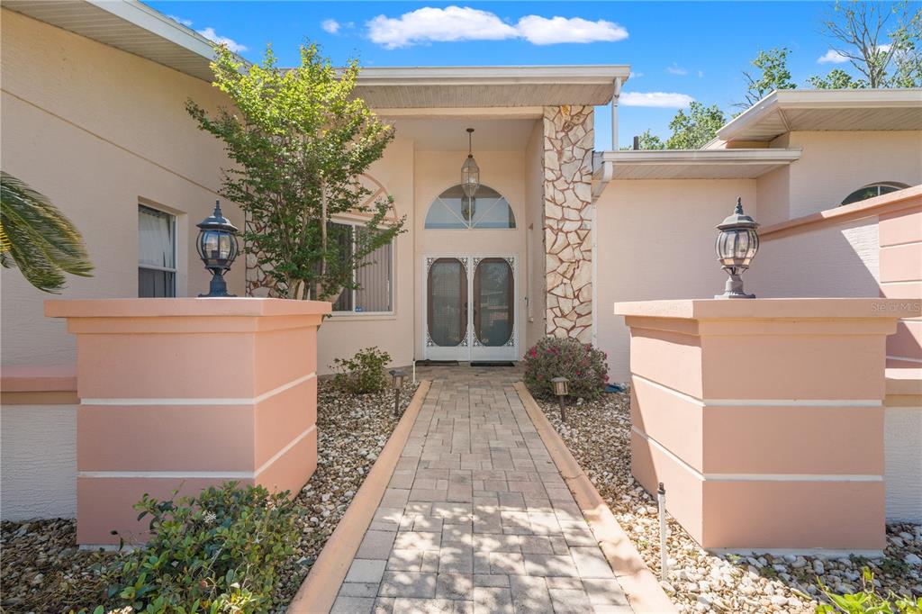 A stone walkway leads to the front entrance of a house with peach-colored stucco walls — 4071 BLACK OAK TRAIL, BROOKSVILLE, FL