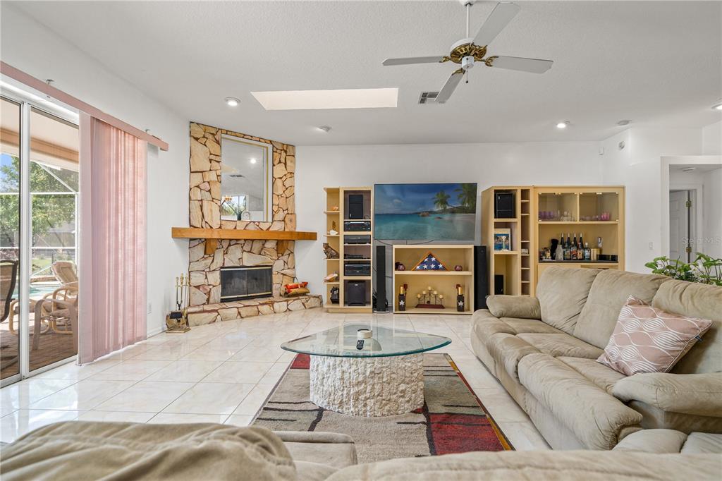 A living room features a stone fireplace, a television, light tile flooring, and a ceiling fan — 4071 BLACK OAK TRAIL, BROOKSVILLE, FL