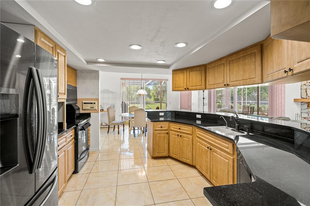 A kitchen with light wood cabinets, black countertops, and tile flooring, opening to a dining area — 4071 BLACK OAK TRAIL, BROOKSVILLE, FL