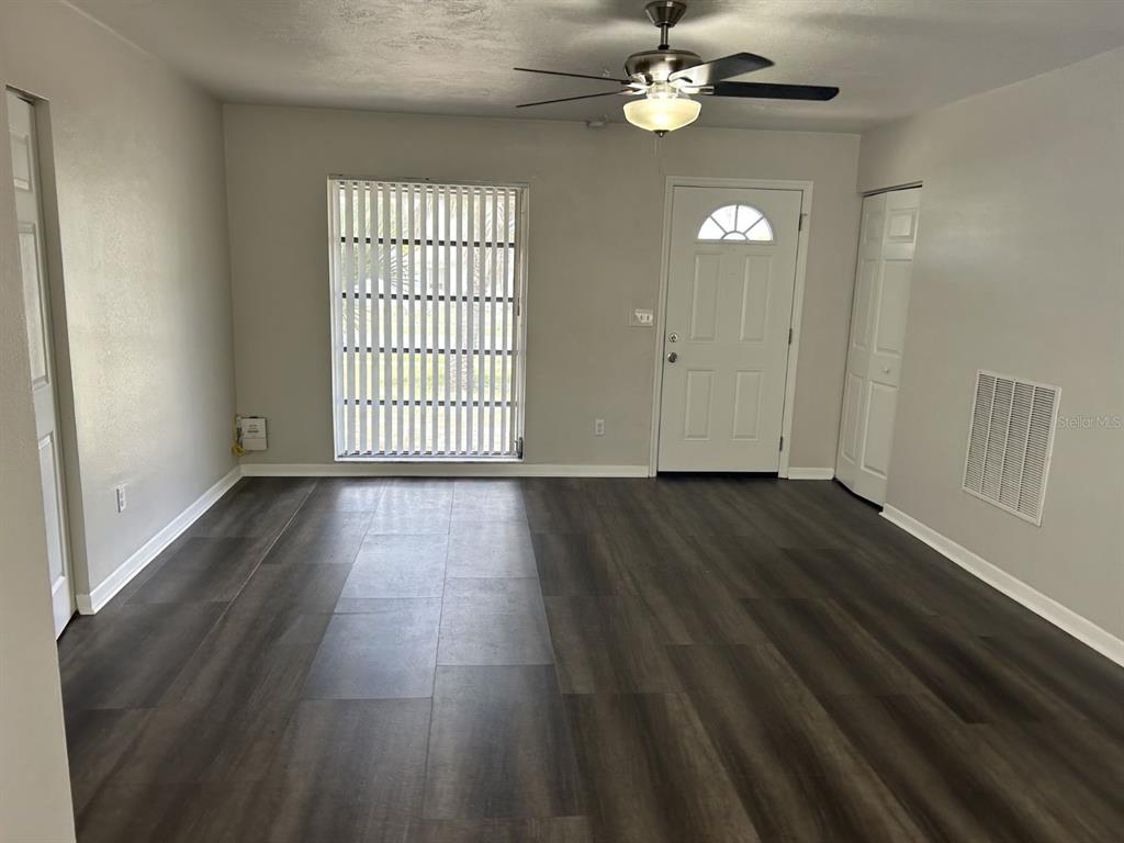 A living room features dark wood-look flooring, a ceiling fan, a front door, and blinds — 1241 PILGRIM RD, SPRING HILL, FL
