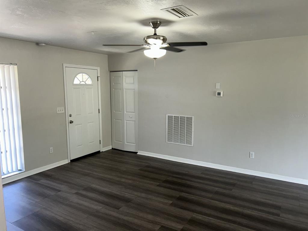 A living room features dark wood-look flooring, a ceiling fan, a white door, and a closet — 1241 PILGRIM RD, SPRING HILL, FL