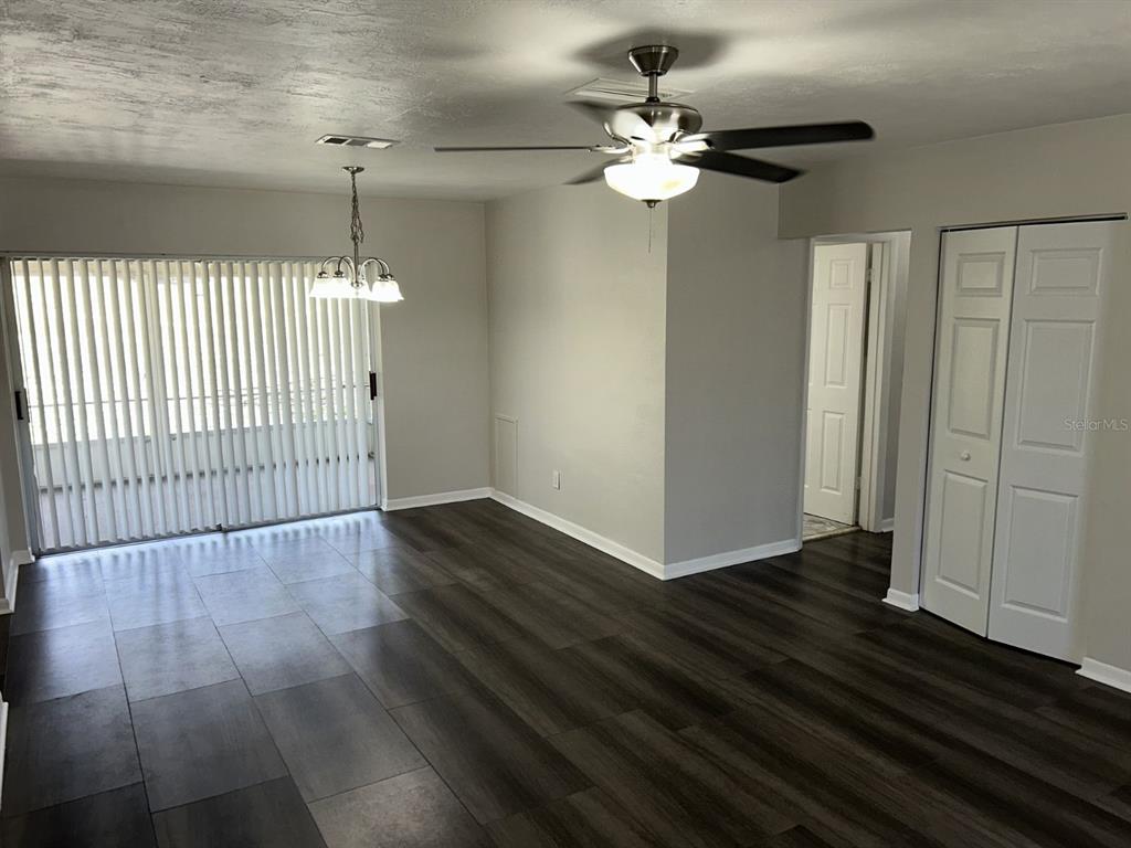 An empty room features dark wood-look flooring, a ceiling fan, and sliding glass patio doors — 1241 PILGRIM RD, SPRING HILL, FL
