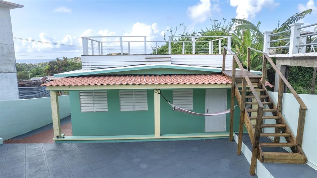 A green house with a tiled roof, a hammock, and wooden stairs leading to a deck — E115 CALLE M-GARCIA, VIEQUES, PR
